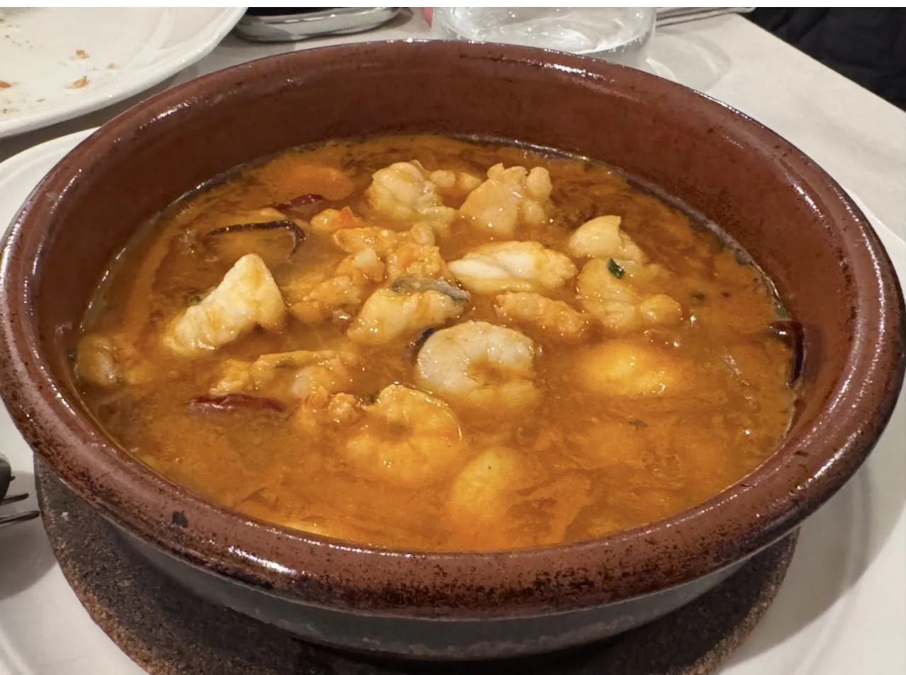 A clay dish of shrimp and seafood in an orange broth