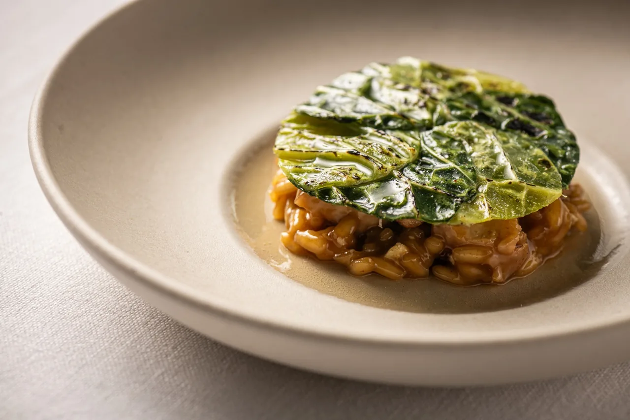 A round layered dish topped with green leaves on a cream plate