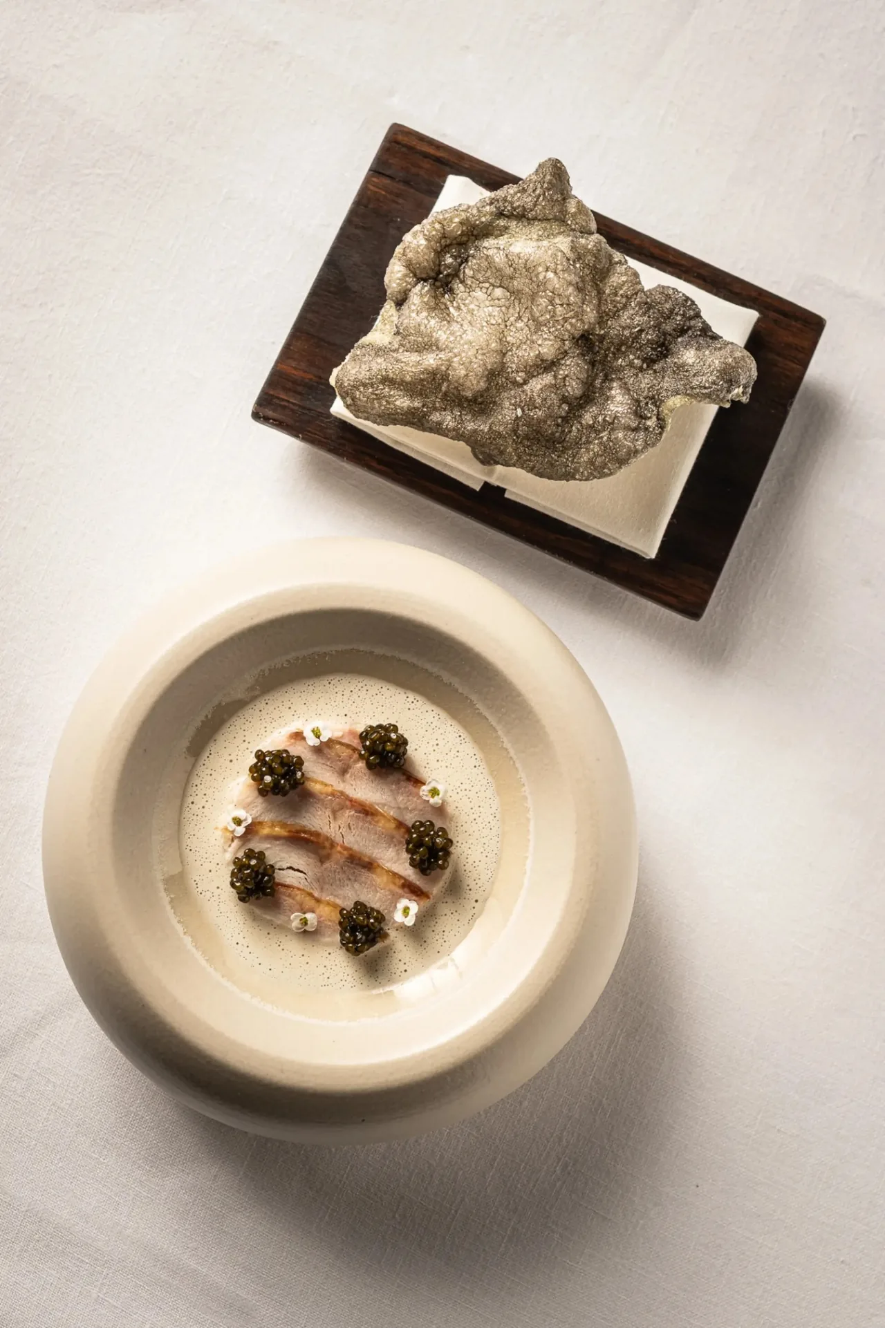 Overhead view of a round bowl of a delicate dish with black dots beside a textured grey piece