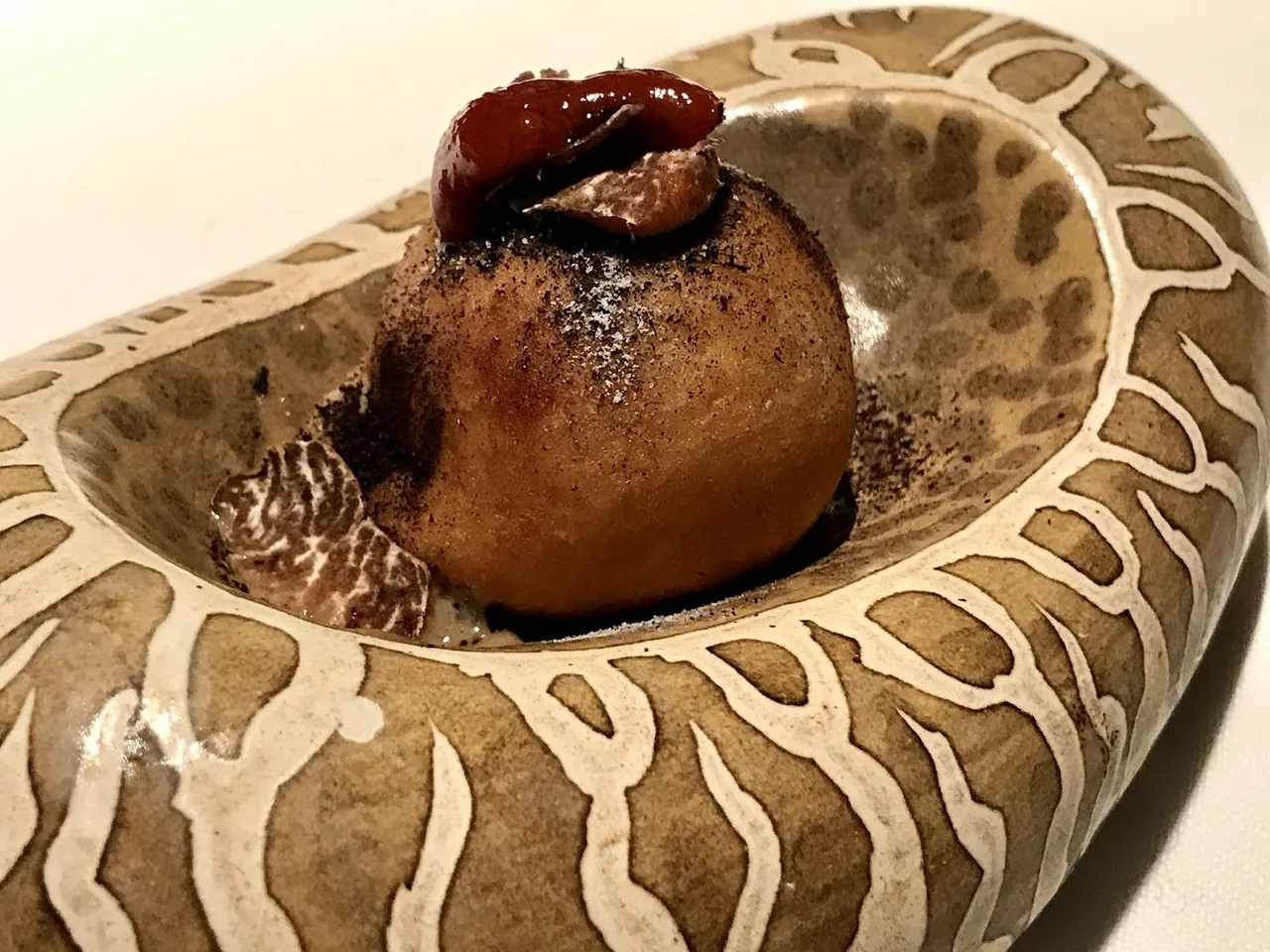 A patterned cream bowl holding a round browned dish with a red topping