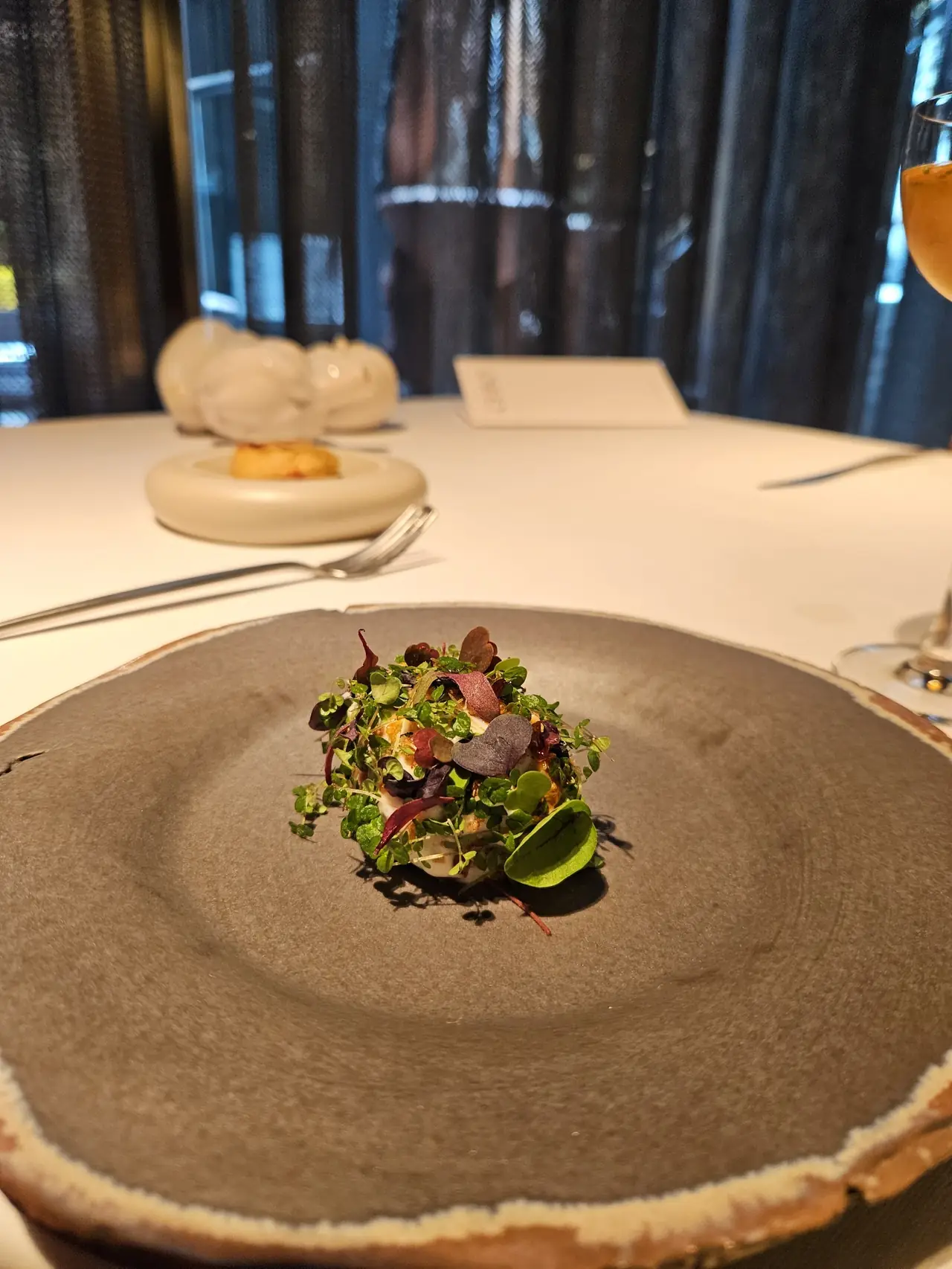 Small dish topped with microgreens and edible flowers on a wide dark stoneware plate