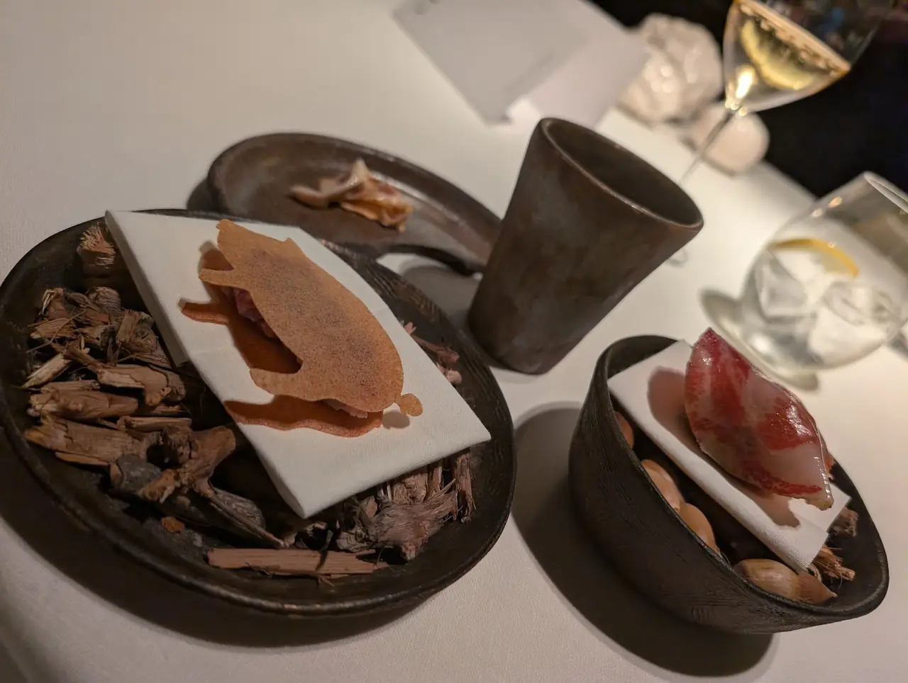 Pig-shaped crisp and cured meat bites served on dark ceramic dishes with wood shavings
