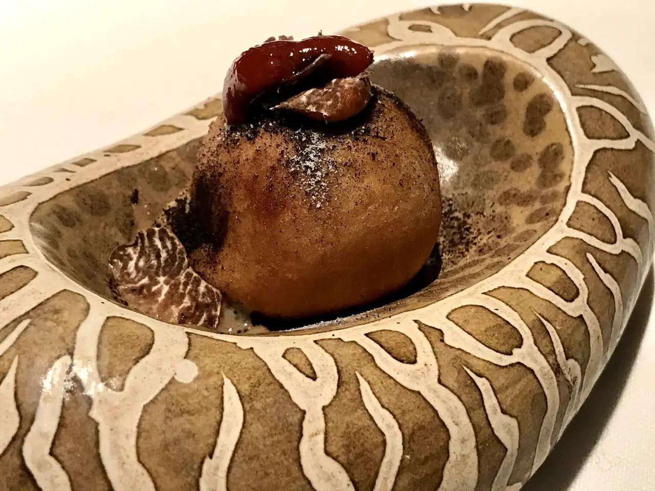 Fried round croquette-like bite with dark sauce and truffle shaving in a patterned bowl