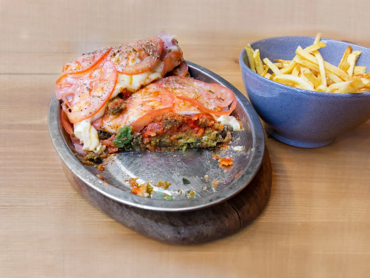 Breaded cutlet topped with melted cheese and tomato slices with a side bowl of fries