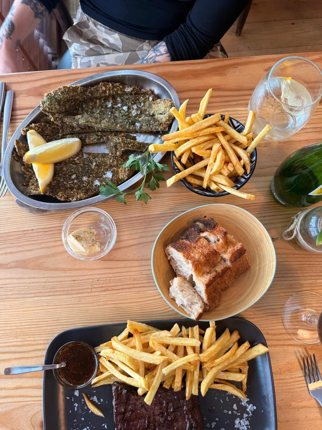 Table spread of breaded fried fish fillets with lemon, french fries, bread and grilled steak