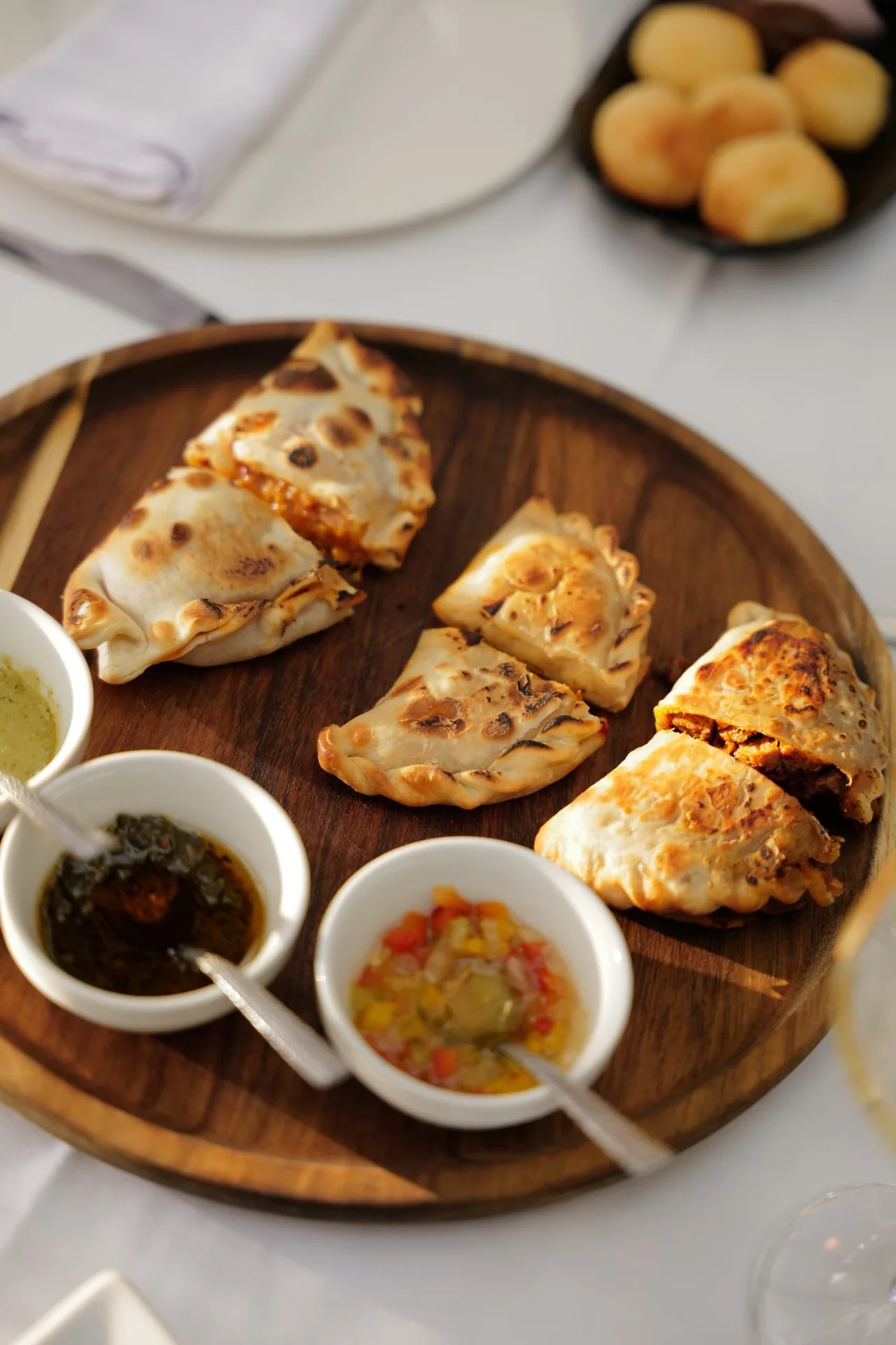 A wooden platter of baked empanadas with bowls of sauces