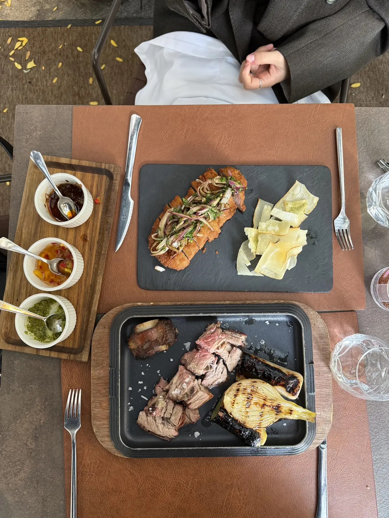 Overhead view of grilled meat with charred leeks and a fried breaded cutlet with onion salad, plus dipping sauces
