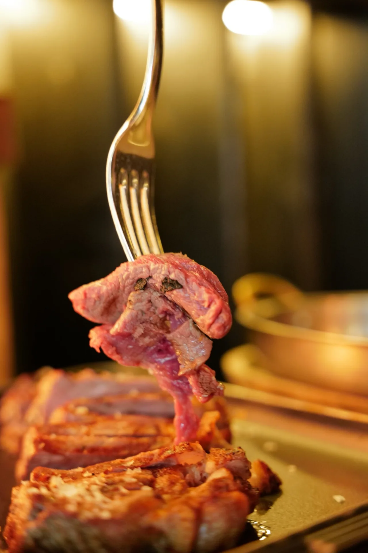 A piece of grilled beef lifted on a fork above a bone-in steak
