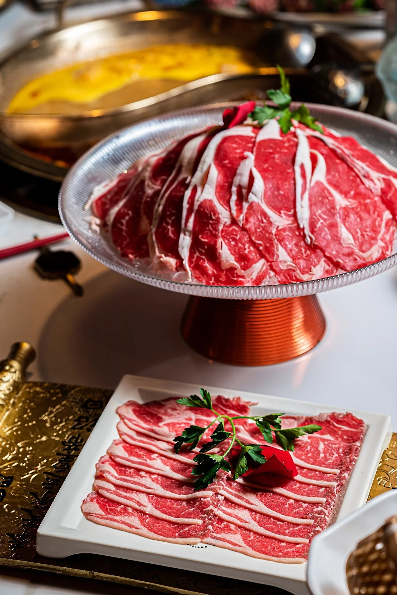 Thin slices of raw beef on a raised metal dish beside a hot pot