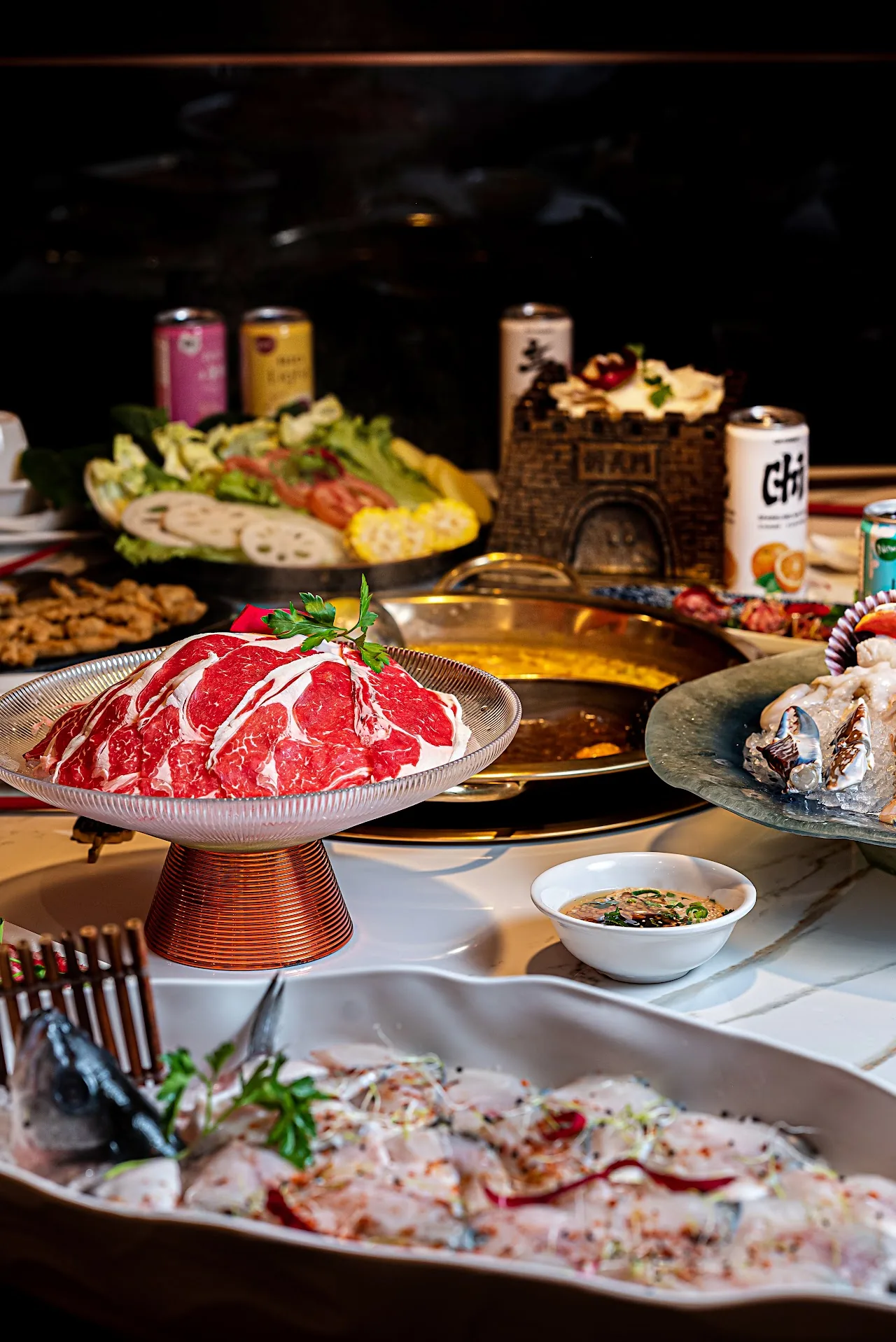 A table spread of hotpot ingredients including sliced meat, vegetables, and sauces