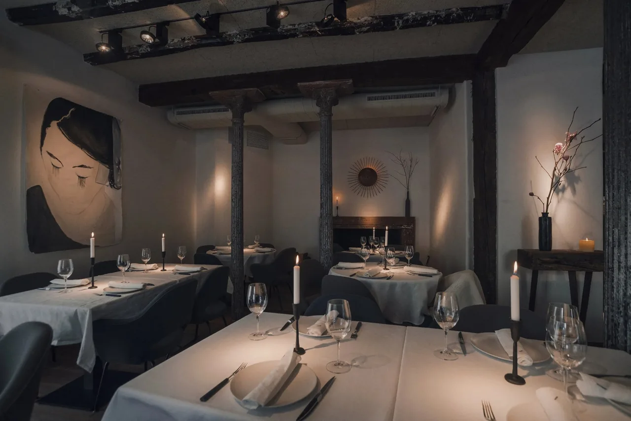 A dining room with white-clothed tables, candles and a large painted portrait on the wall
