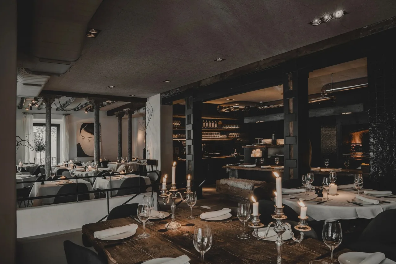 A dark dining room with a candelabra on a wooden table and an open kitchen behind