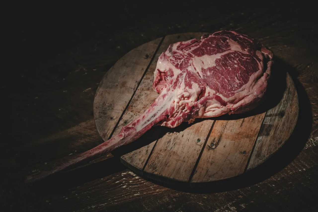 A raw tomahawk steak on a round wooden board in low light