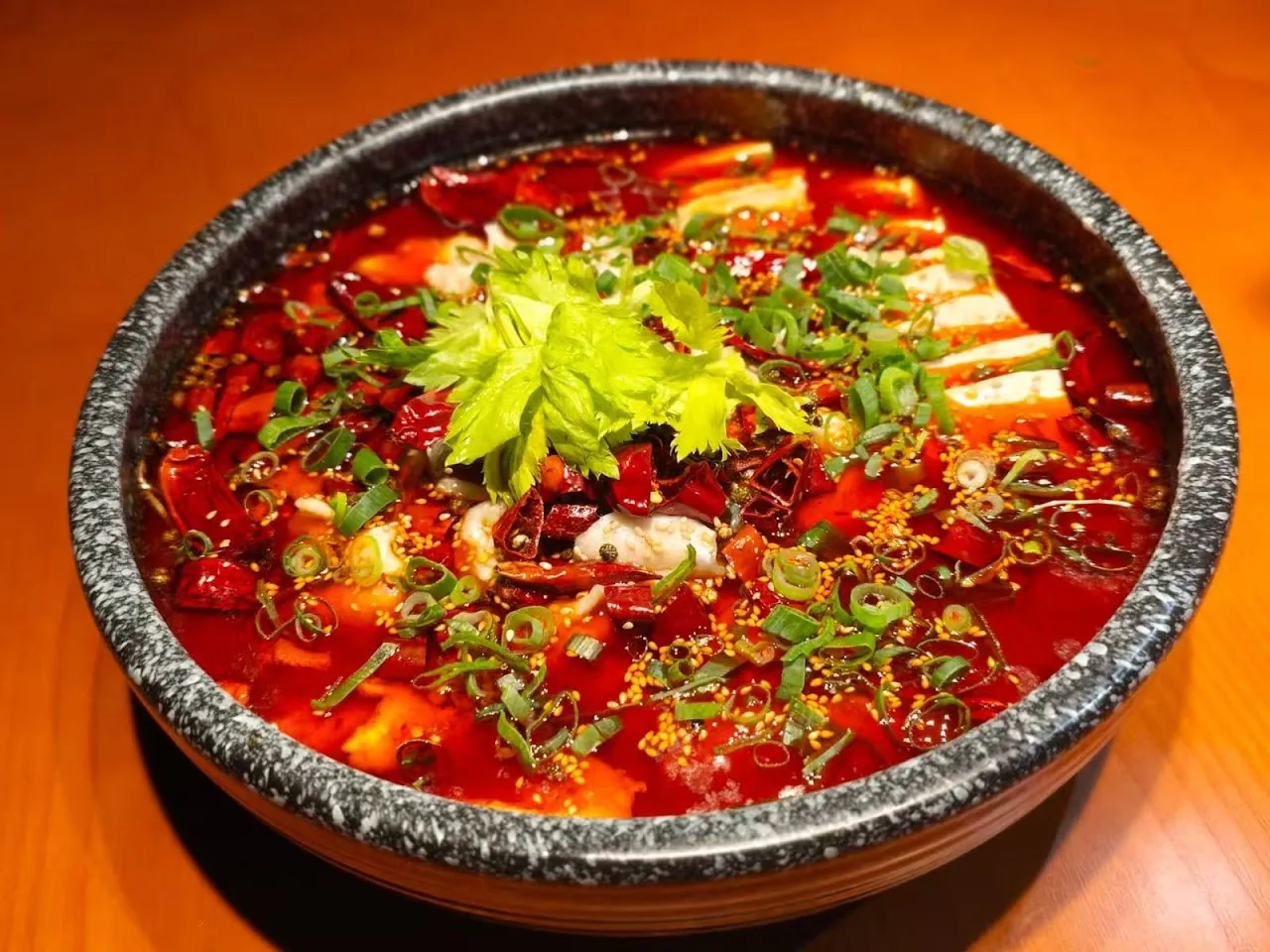 A bowl of spicy red broth with tofu, cilantro, and scallions