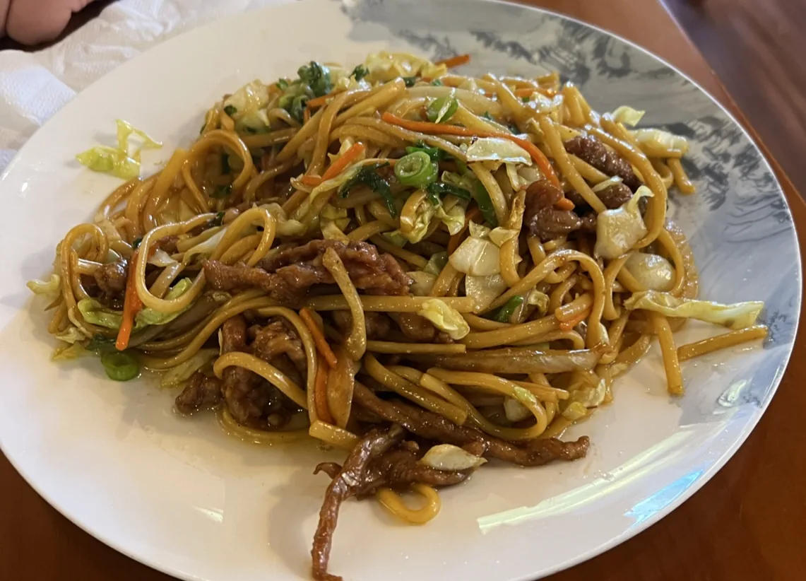 A plate of stir-fried noodles with cabbage and meat