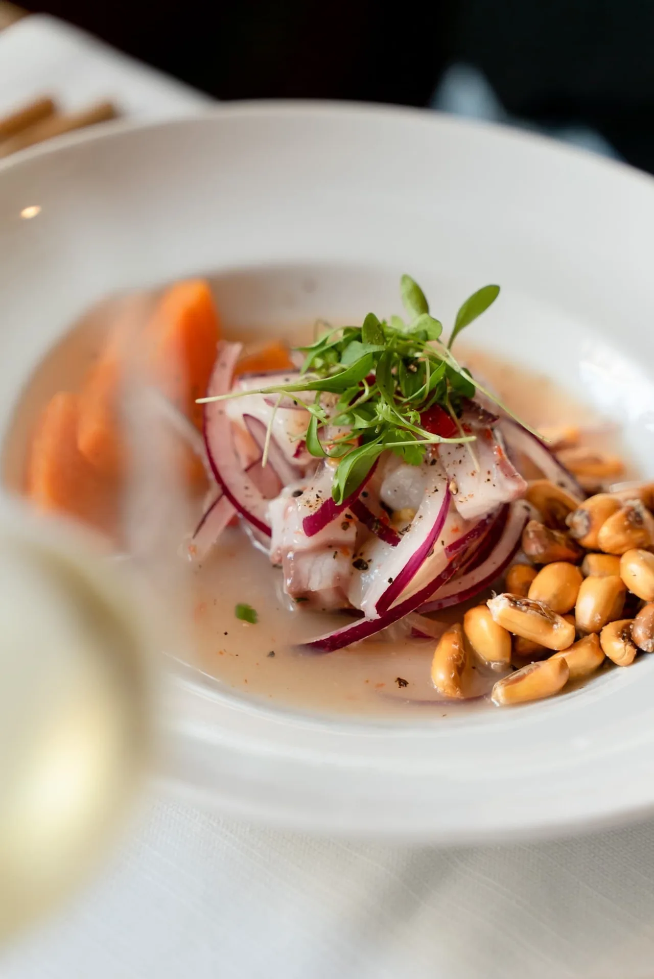 A white plate of ceviche with red onion, carrot and toasted corn kernels