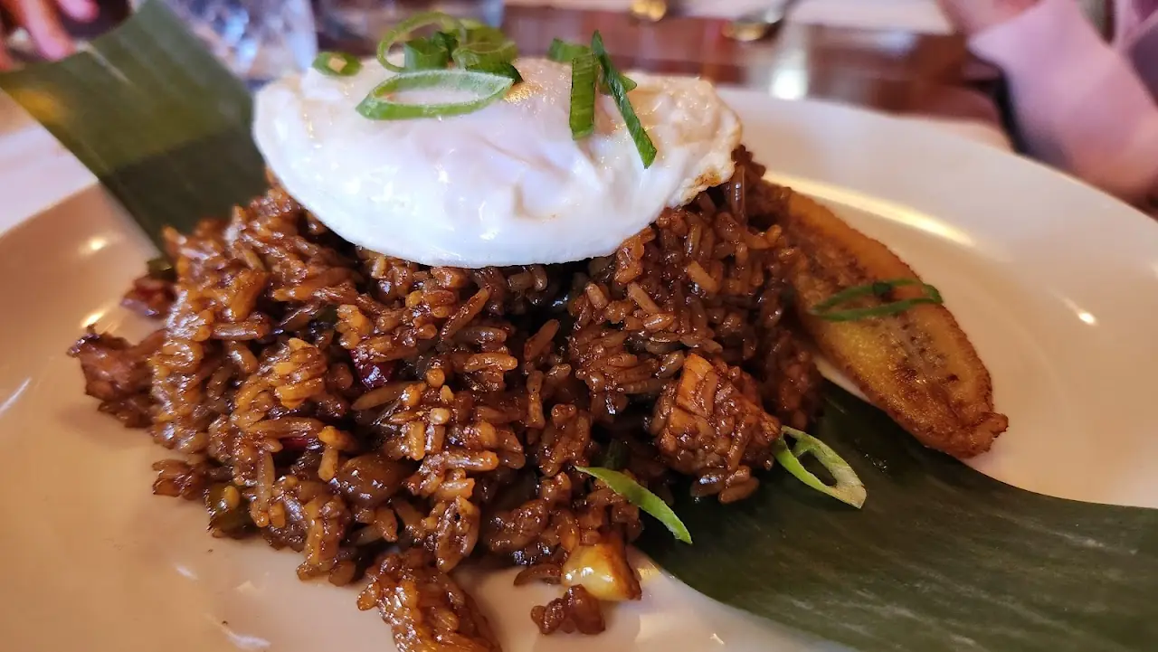 Dark fried rice on a banana leaf, topped with a fried egg and spring onion