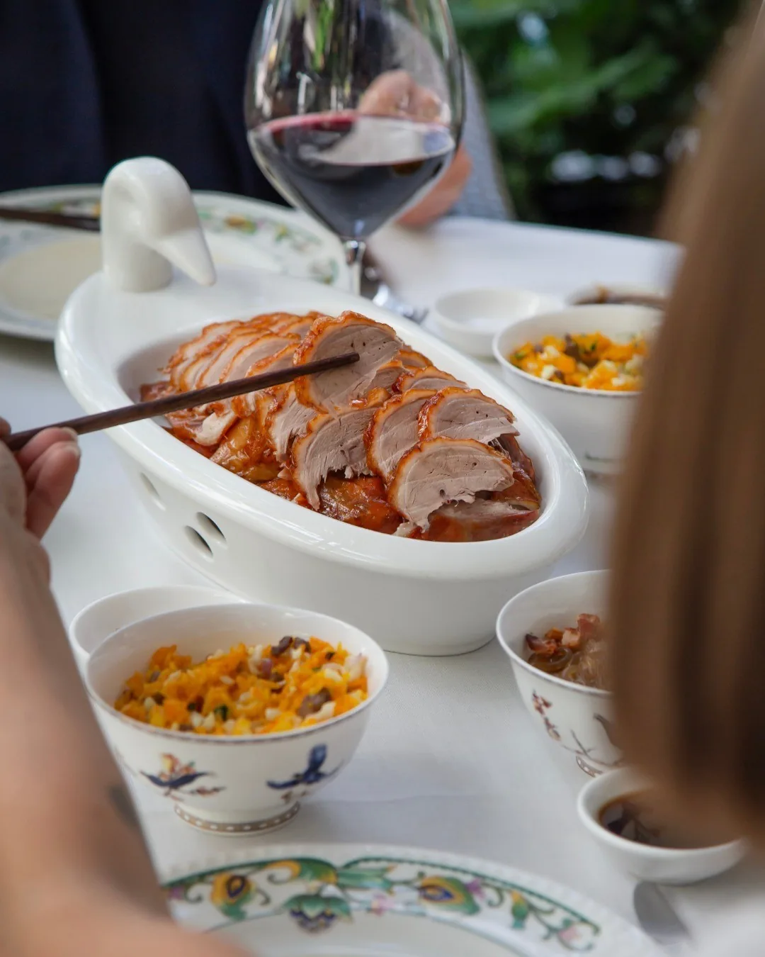 Sliced roast duck on a white oval dish with small bowls of accompaniments