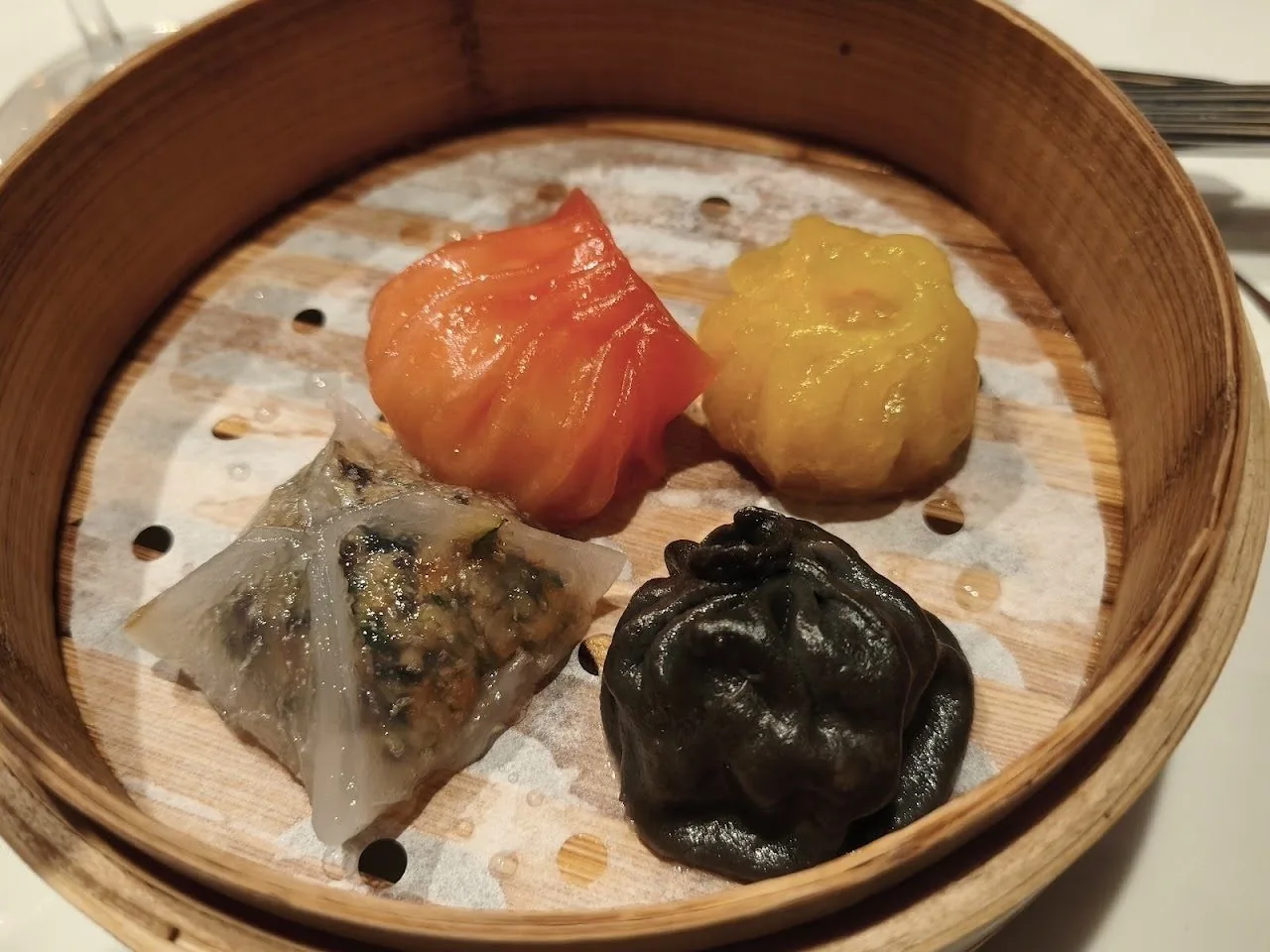 A bamboo steamer holding four colourful dumplings