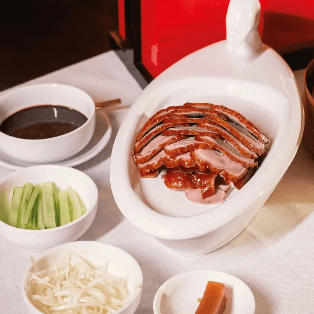 Sliced roast duck on a white dish with cucumber and sauces