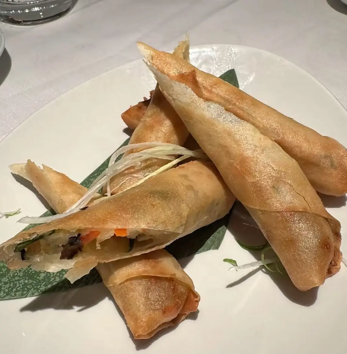 Crispy fried spring rolls stacked on a plate with a garnish leaf.