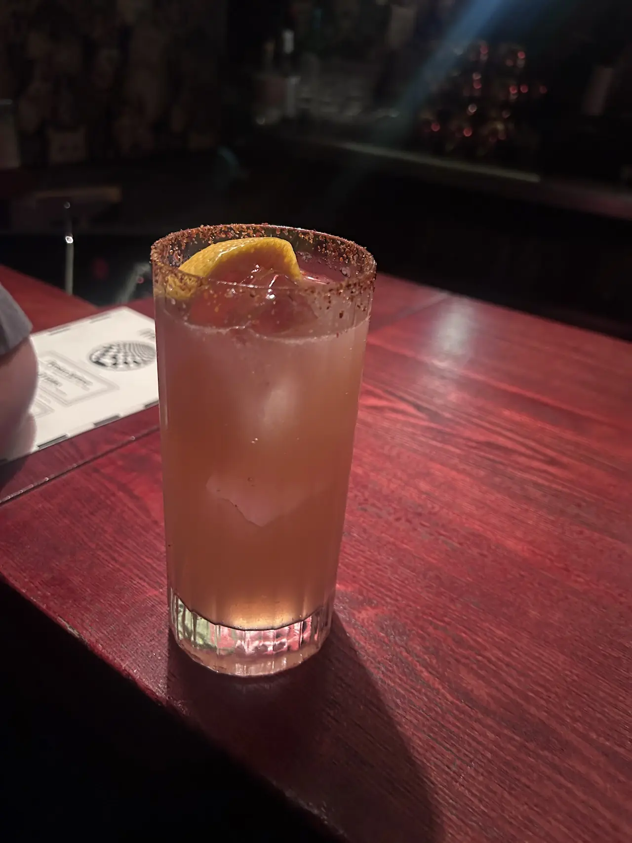 A cocktail garnished with an orange twist, served on a wooden bar counter.