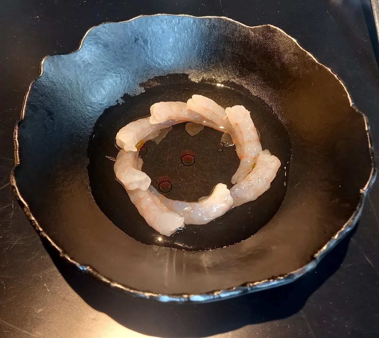 A ring of pale prawns in a dark bowl on a table