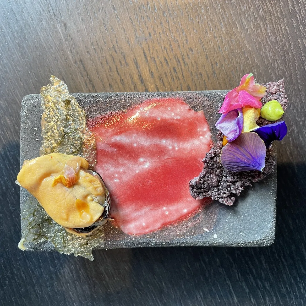 A slate plate with slices of raw red tuna, a golden piece and edible flowers