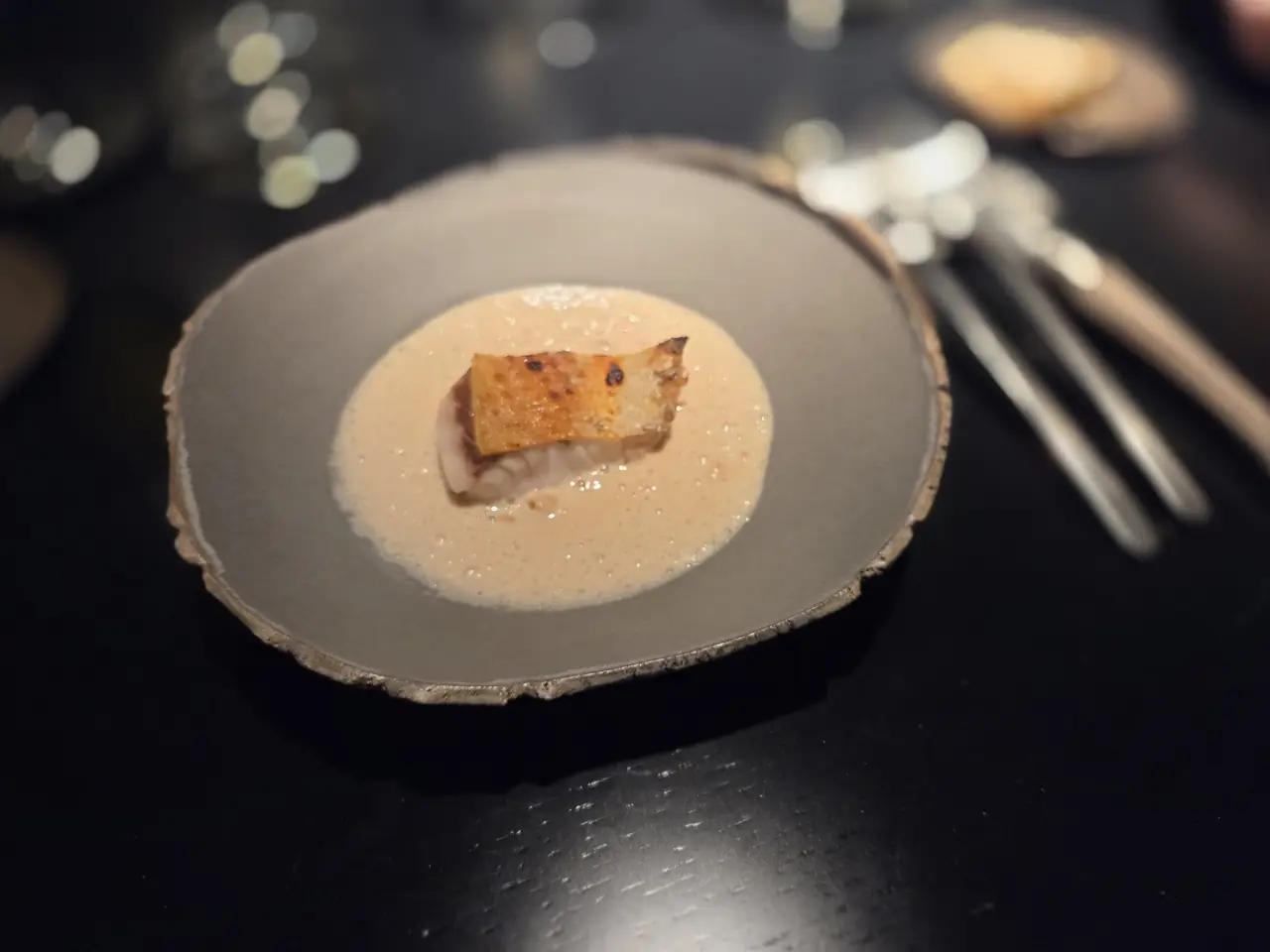 Plated piece of crispy-skinned fish in a creamy foamy sauce on a grey plate