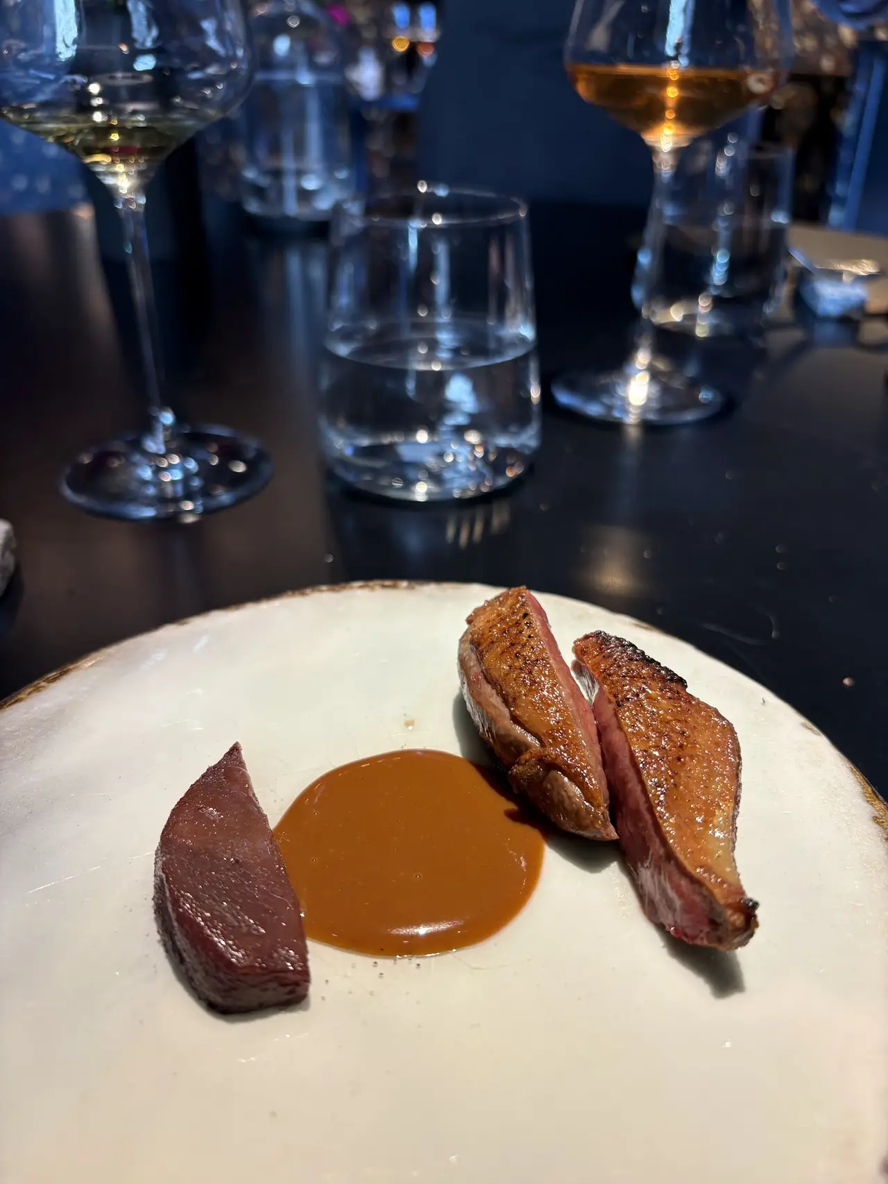 Plated seared duck breast slices with a pool of brown jus sauce on a white plate