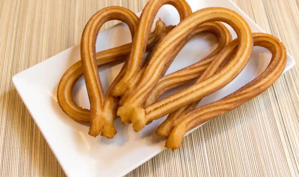 Loops of golden churros on a square white plate on a bamboo mat