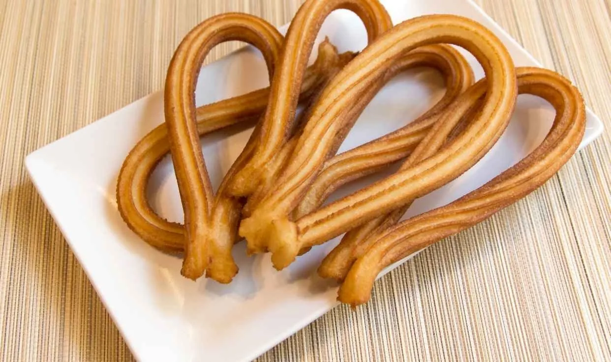 Looped churros on a white rectangular plate on a light wooden table