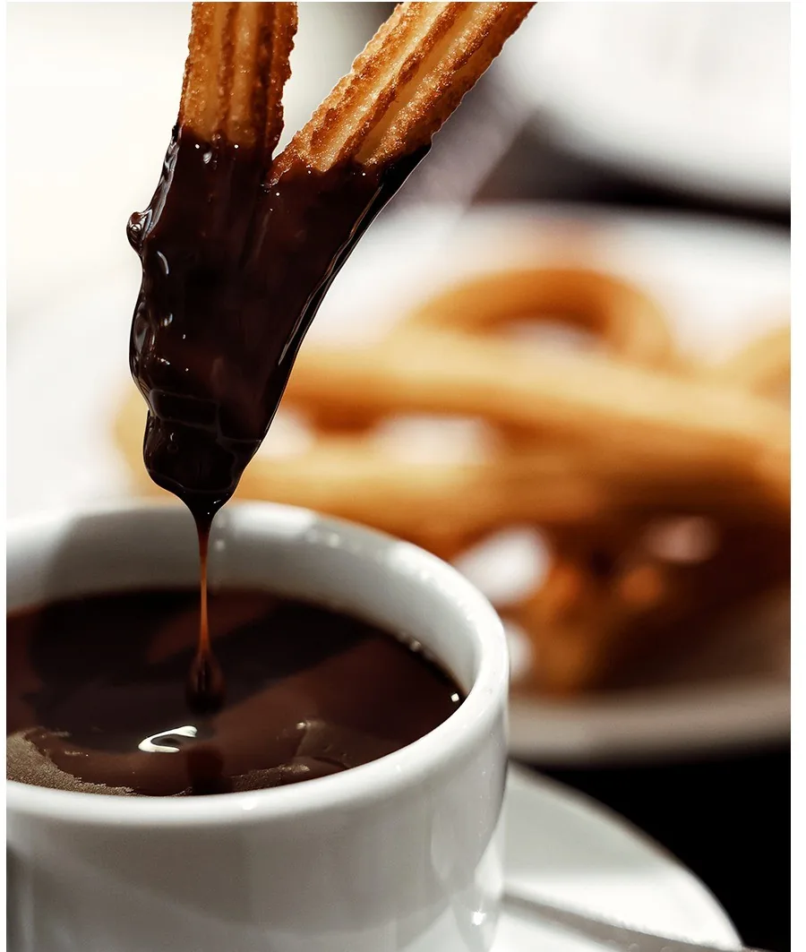 Chocolate being poured into a cup with churros in the background