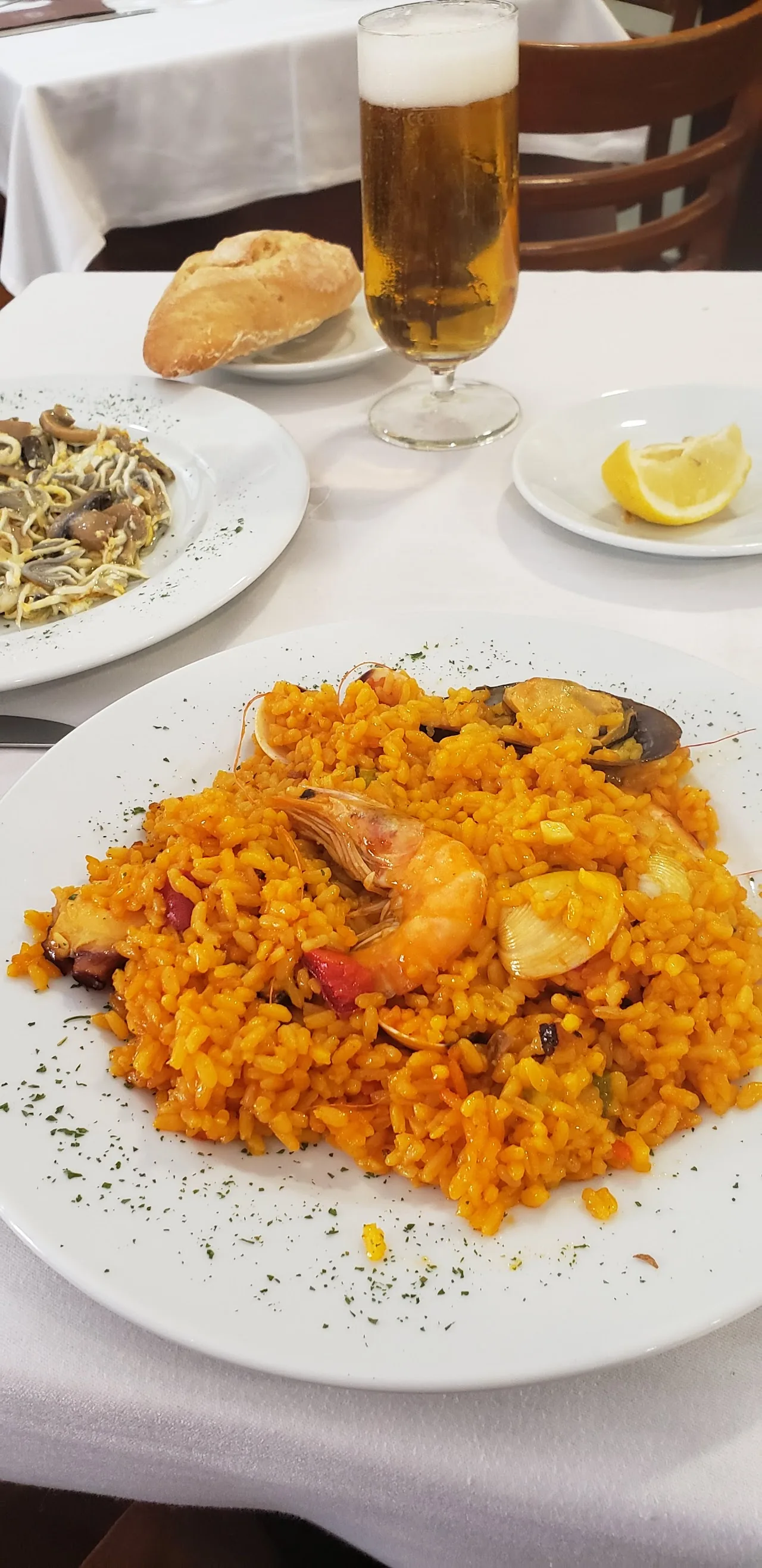 A plate of seafood paella with shrimp, served with beer