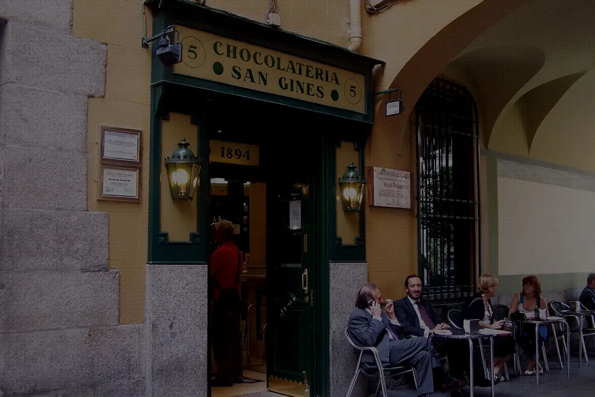 Green-and-cream storefront of Chocolateria San Gines with its painted sign, twin lanterns marked 1894 and patrons seated at outdoor terrace tables