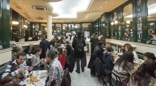 Busy interior dining room with green-and-white marble decor, mirrored walls, framed photos and crowds of patrons seated at tables