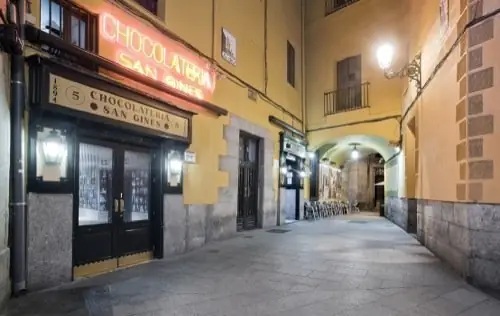 Night exterior of the venue on a cobbled lane with its illuminated neon Chocolateria San Gines sign above the dark green doors