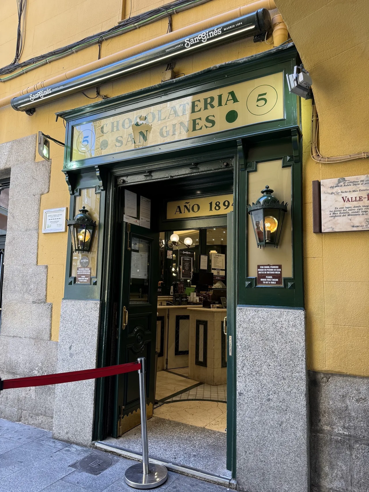 A green and yellow shopfront entrance with lanterns and a red rope in front of the door