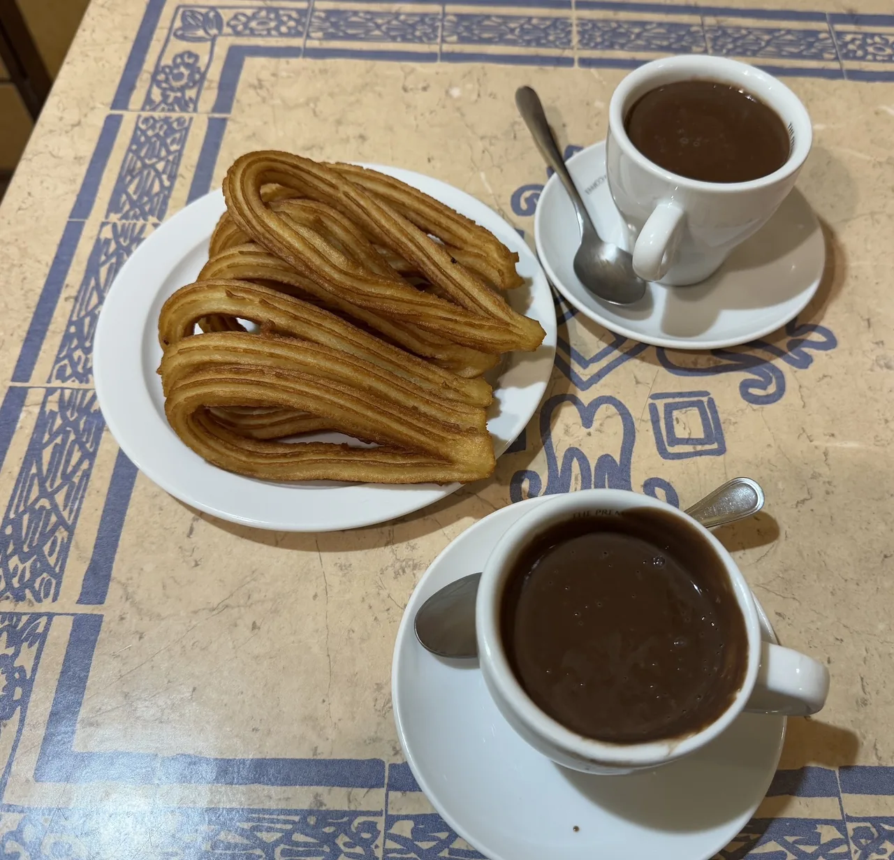 A plate of churros beside a cup of hot chocolate on a tiled table