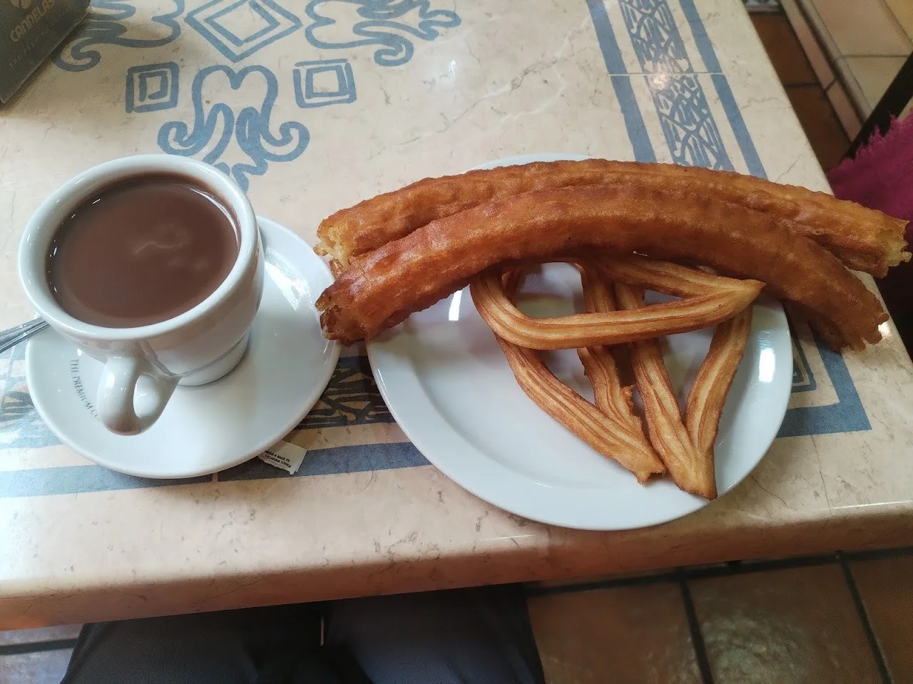 A plate of churros beside a cup of chocolate on a patterned table