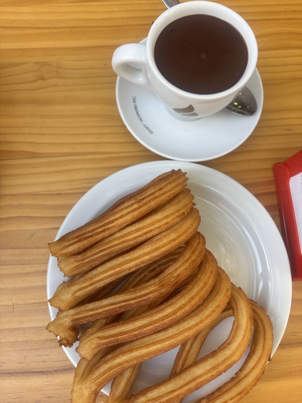 A plate of churros seen from above beside a cup of chocolate on a wooden table