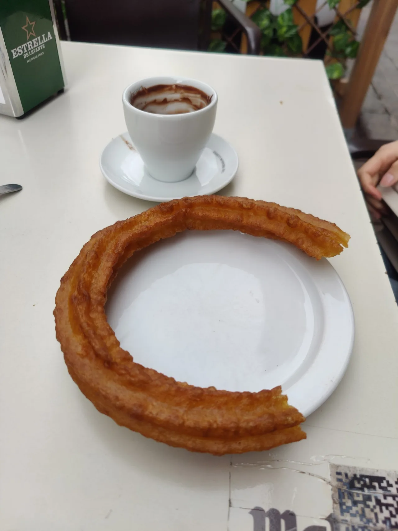 A ring-shaped churro on a white plate beside a cup of chocolate