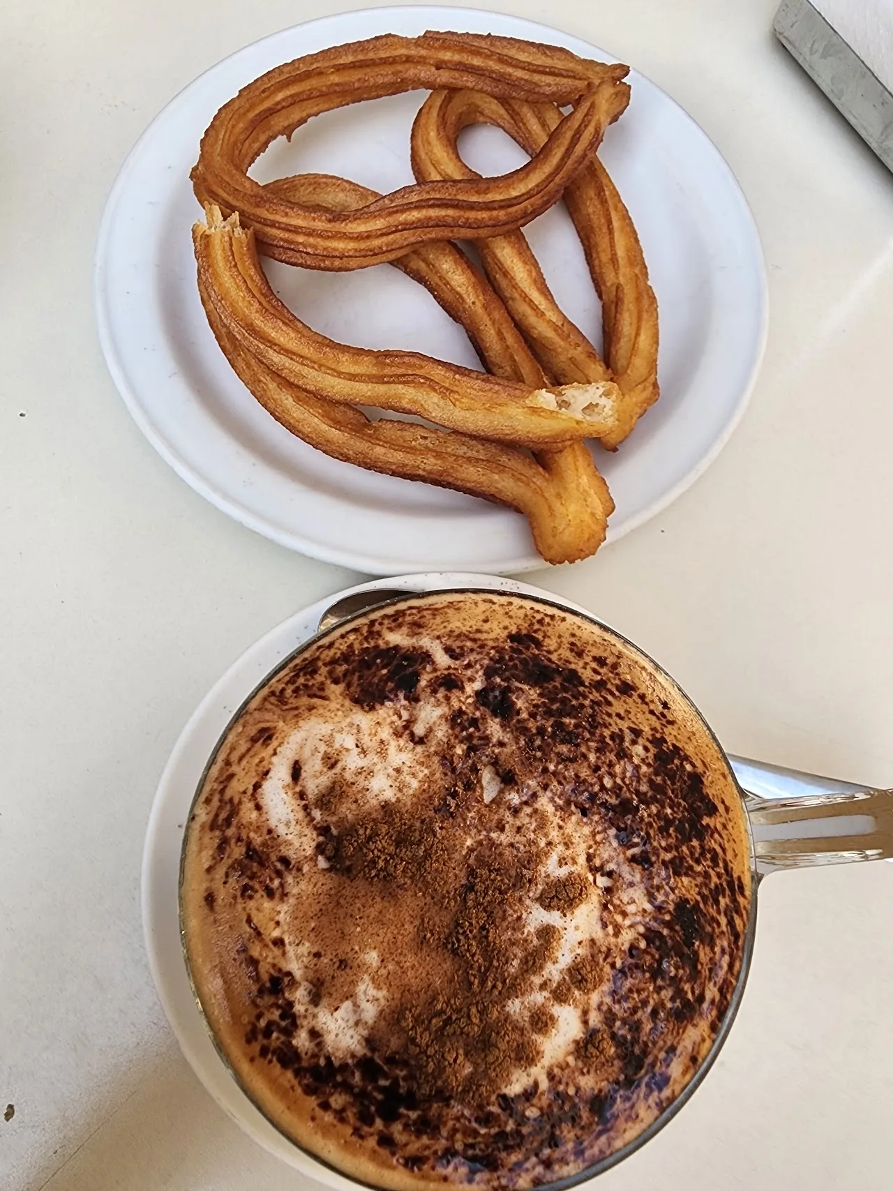 A coil of churros beside a mug of thick hot chocolate topped with cream