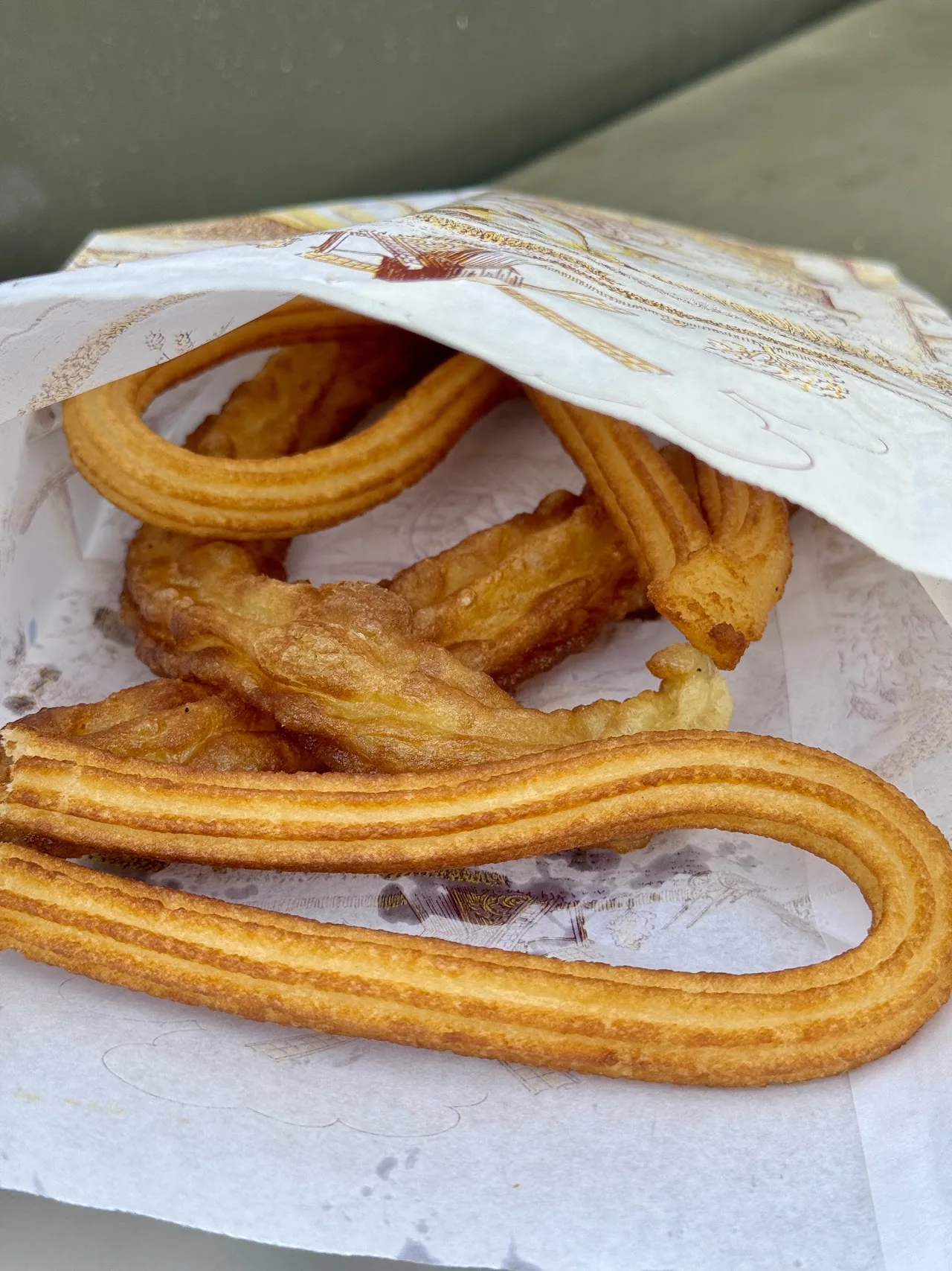A paper-wrapped bundle of churros drizzled with chocolate sauce