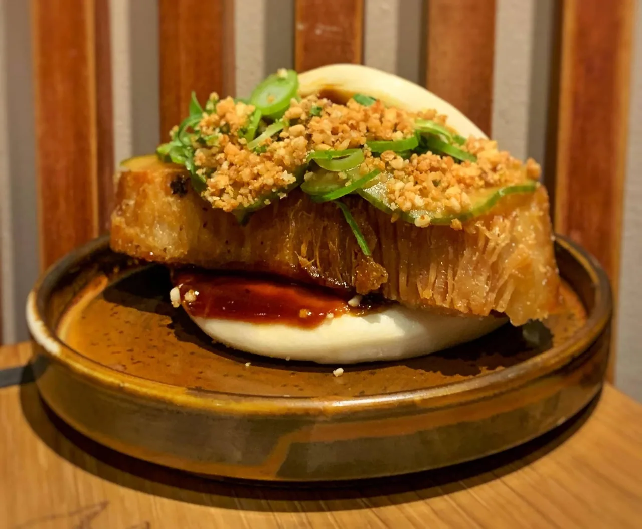 A steamed bun filled with crisp topping and dark sauce on a round brown plate