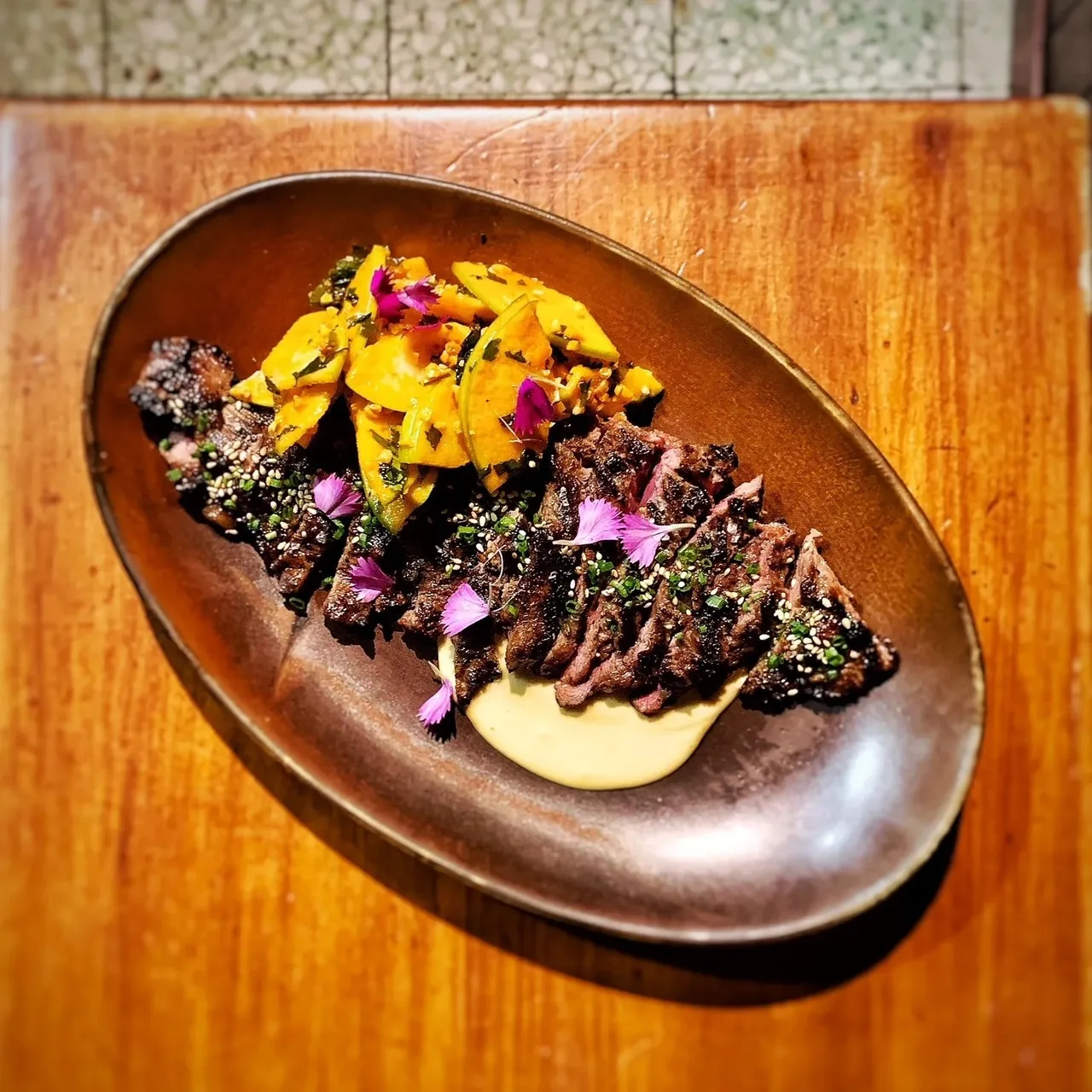 Sliced meat with orange and purple garnishes on an oval dark plate on a wooden table