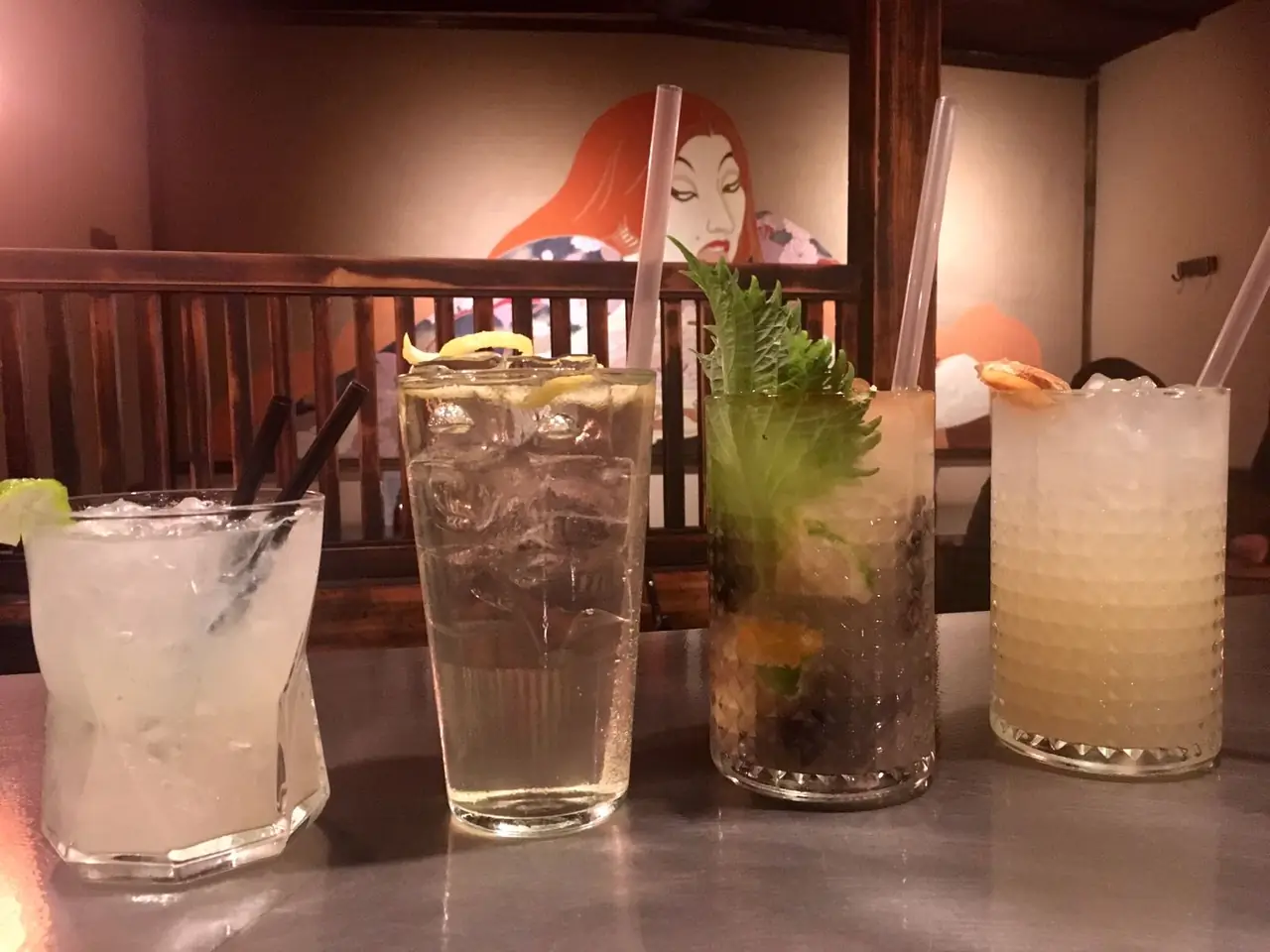 Four cocktails in glasses with ice, citrus and herb garnishes lined up on a table