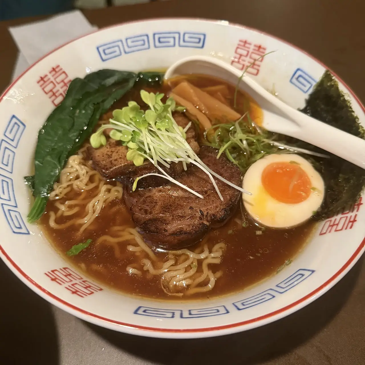 Bowl of ramen with sliced pork, soft egg, bamboo shoots, nori and greens in brown broth