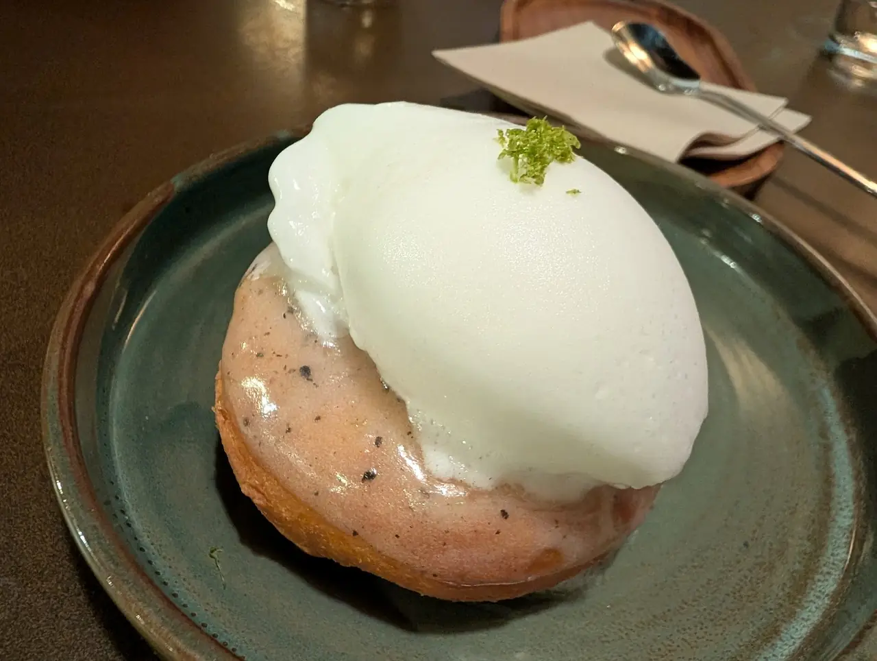 Glazed bun dessert topped with cream and lime zest on a plate