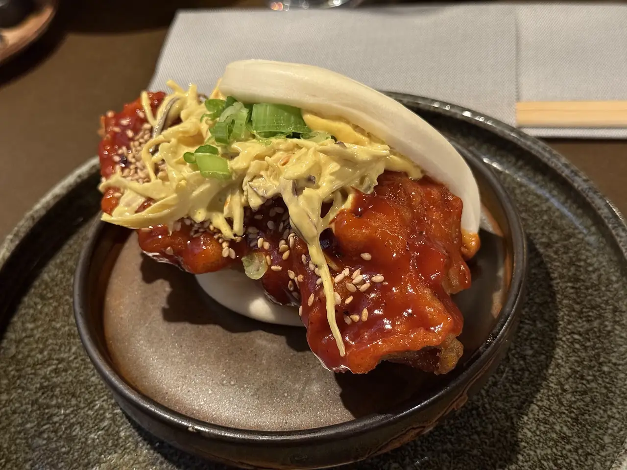 Steamed bao bun filled with glazed fried chicken, slaw and sesame seeds on a plate
